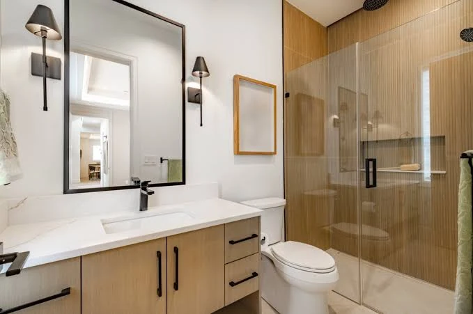 Compact bathroom with an oak vanity and a glass shower enclosure with wood-look tile