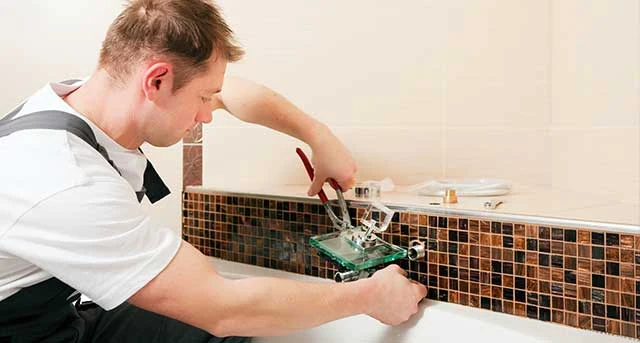 Illustrative photo of a person adjusting a bathtub faucet above a mosaic backsplash