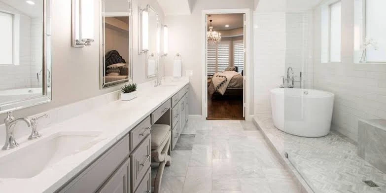 Bright bathroom with a long gray vanity, marble flooring and a freestanding oval bathtub