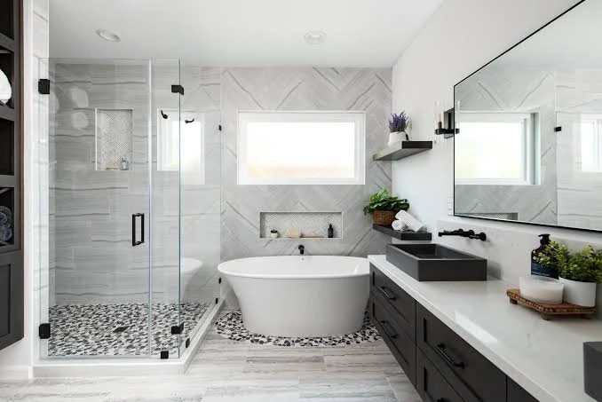 Bathroom with gray herringbone wall tile, pebble accents, a white tub and a black vanity