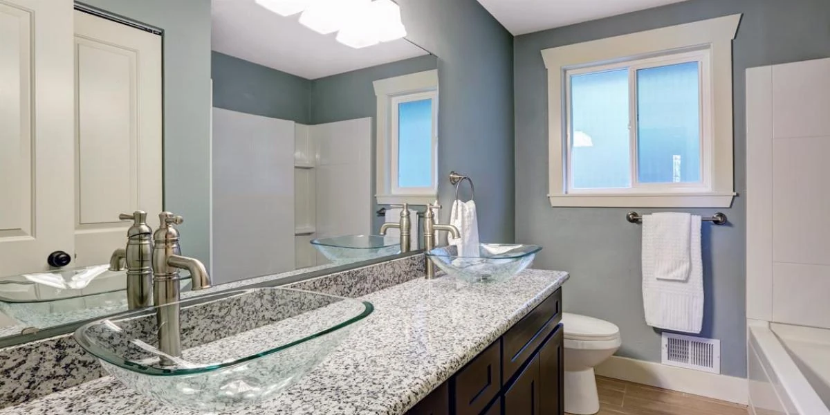 Double bathroom vanity with glass vessel basins, granite countertop and a large wall mirror